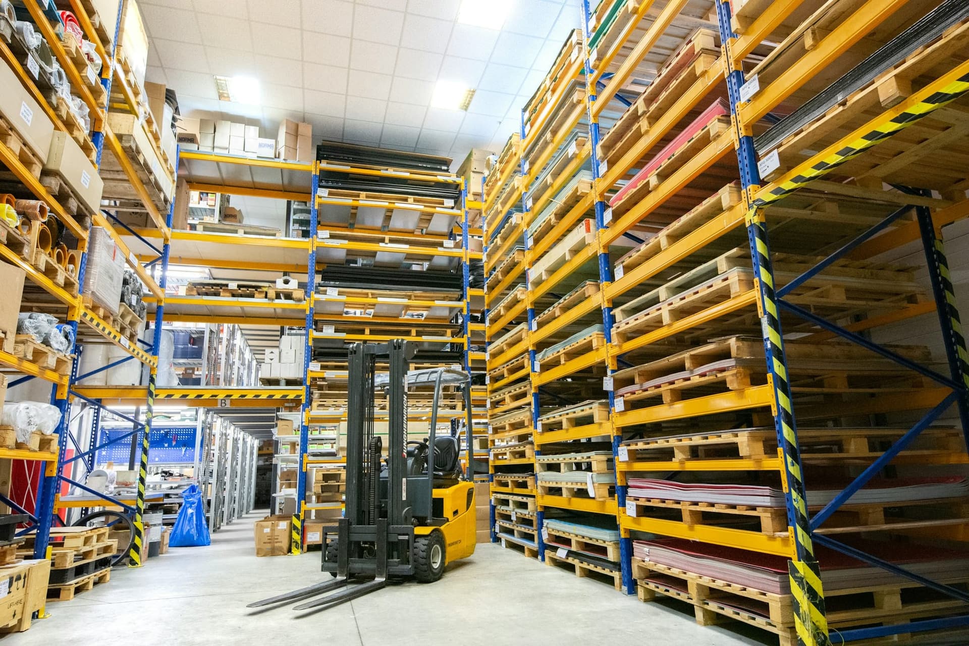 Forklift moving wooden pallets between racking in a wholesale warehouse