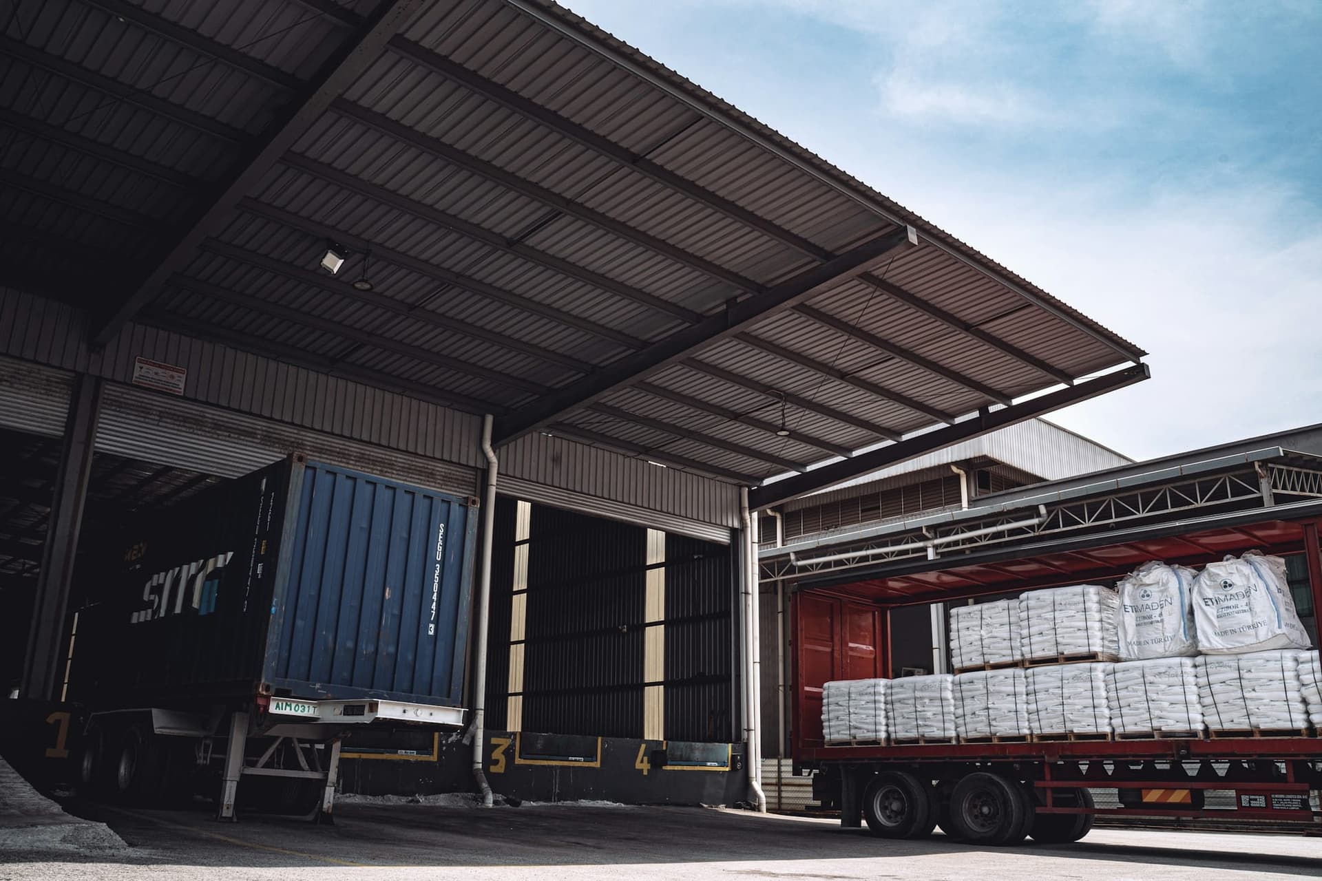 Shipping container and freight trailer being loaded at a warehouse bay